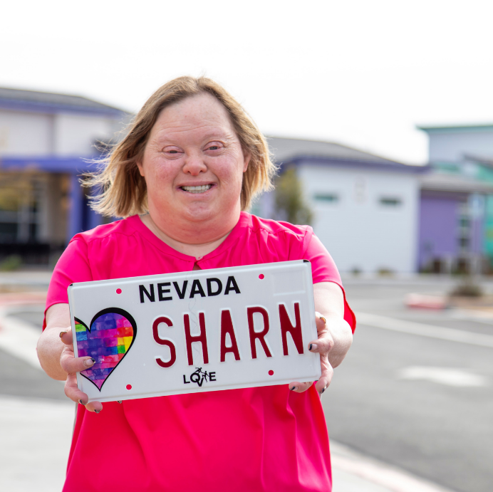 Artist, Sharon, holding her design of the Opportunity Village charity license plate.