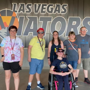 group of six people standing and sitting in front of a last vegas aviators sign