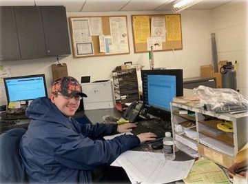 person sitting in an office at a desk in front of a computer while smiling at the camera