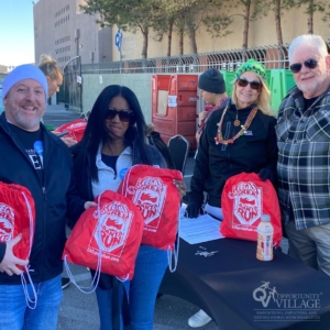 four people standing at a charitable event table holding red backpacks with Santa on them