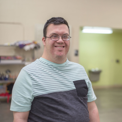 man in a t-shirt smiling at the camera while standing in a warehouse