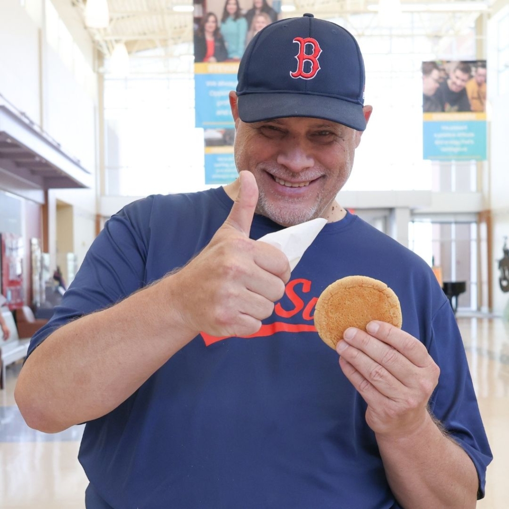 person holding a cookie in one hand and giving a 'thumbs up' with the other.