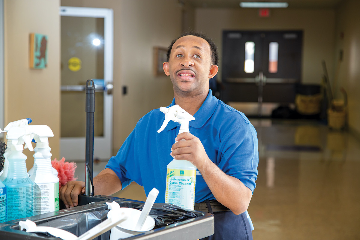 personal holding a spray bottle standing next to a commercial cleaning cart in a hallway