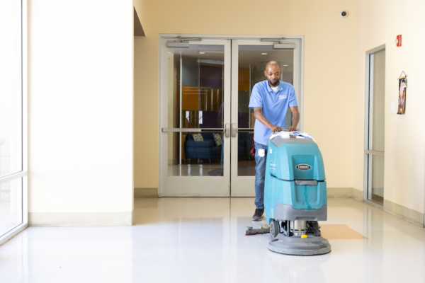 personal working a commercial cleaning floor cleaner in a hallway