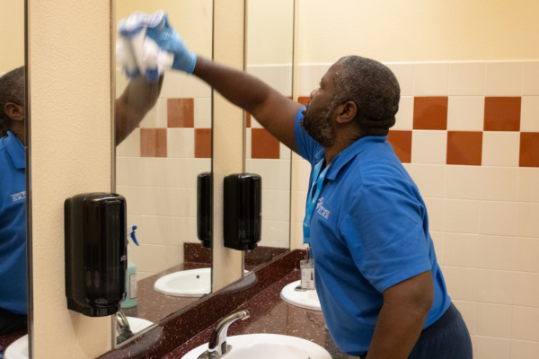 person providing commercial cleaning service in a public restroom, cleaning a mirror